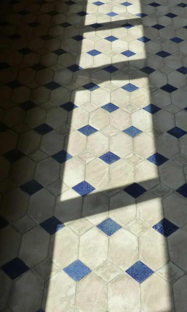 Sol de carreaux hexagonaux clairs à cabochons bleus traversé par une bande de soleil