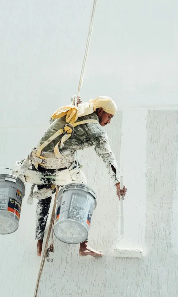 Peintre suspendu le long d’un grand mur blanc, seaux de peinture à la main