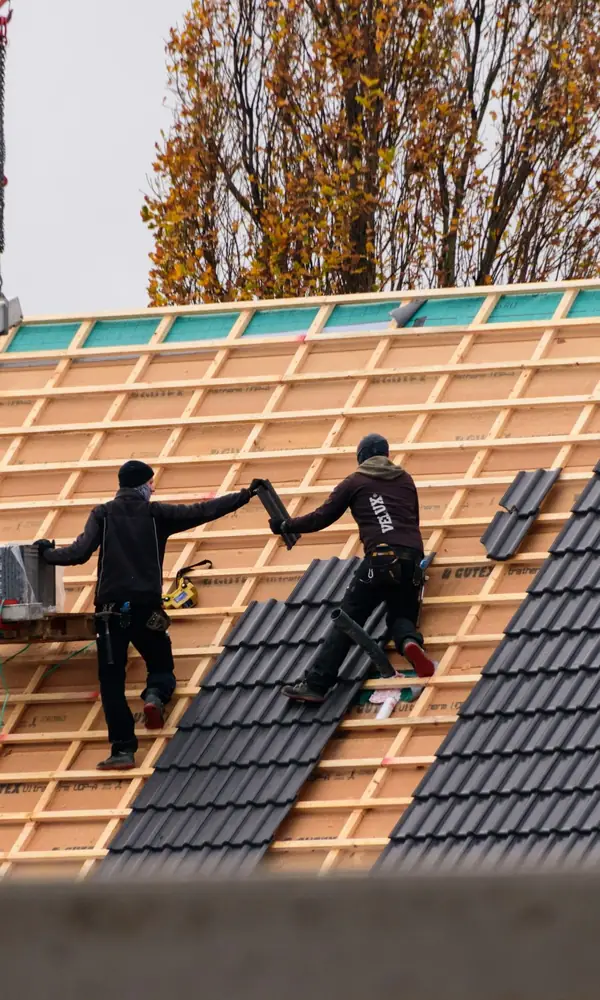 Deux couvreurs posent des tuiles sombres sur des liteaux neufs