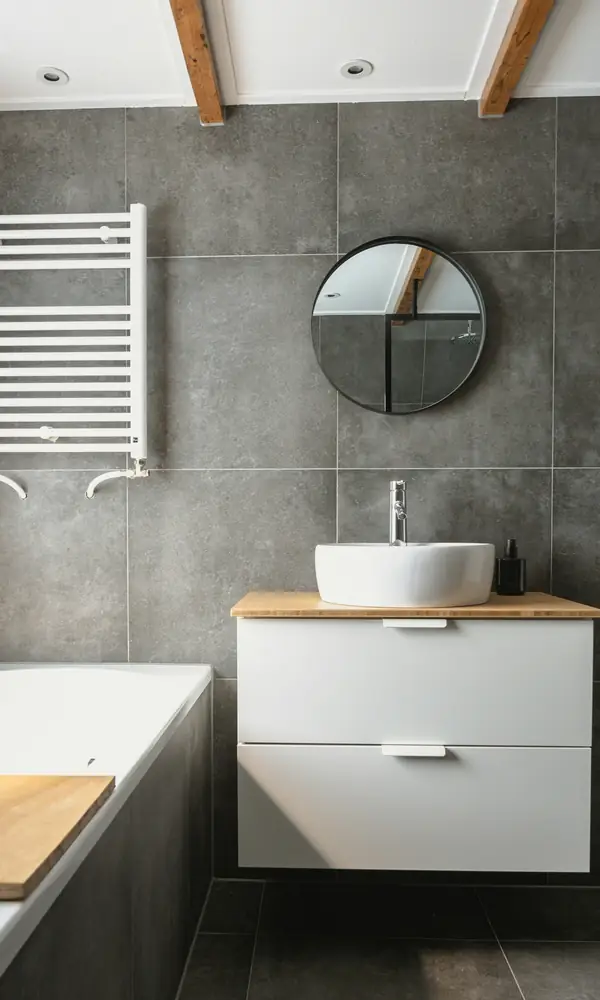 Salle de bain en grands carreaux gris, vasque blanche, sèche-serviettes et baignoire